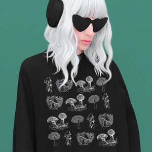 May include: A black sweatshirt with a white graphic print of mushrooms. The model is wearing black headphones and sunglasses.