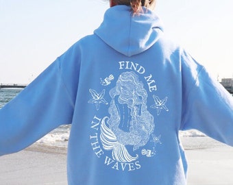 Peut inclure: Un sweat-shirt bleu clair avec un motif blanc de sirène et le texte "Find Me In The Waves".