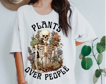 Pode incluir: Camiseta branca com um gráfico preto de um esqueleto rodeado de plantas e o texto "Plants Over People".