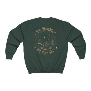 May include: A dark green sweatshirt with a graphic print on the back. The graphic features a mountain range, a crescent moon, stars, and the text "The Universe Has Your Back".