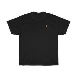 Pode incluir: T-shirt preto com um pequeno desenho dourado de lua crescente e estrelas no lado esquerdo do peito. A camisa &eacute; feita de um material macio e confort&aacute;vel, adequado para uso casual. O design &eacute; simples e elegante.