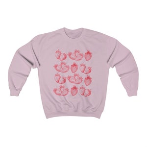 May include: A pink sweatshirt with a repeating pattern of red strawberries. The strawberries are drawn in a vintage style.