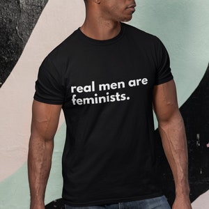 May include: A black t-shirt with the text "real men are feminists." printed in white on the front.