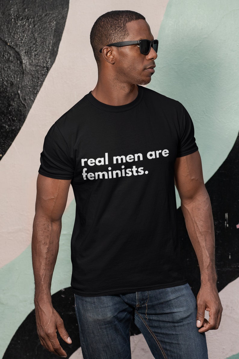 May include: A black t-shirt with the text "real men are feminists." printed in white on the front.