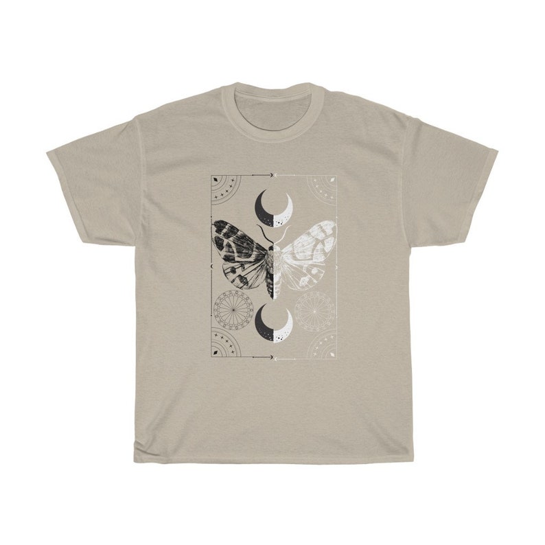 K&ouml;nnte beinhalten: Ein beiges T-Shirt mit einem schwarzen und wei&szlig;en Mottivendesign. Der Falter befindet sich in der Mitte eines quadratischen Rahmens mit geometrischen Mustern und Mondsicheln.