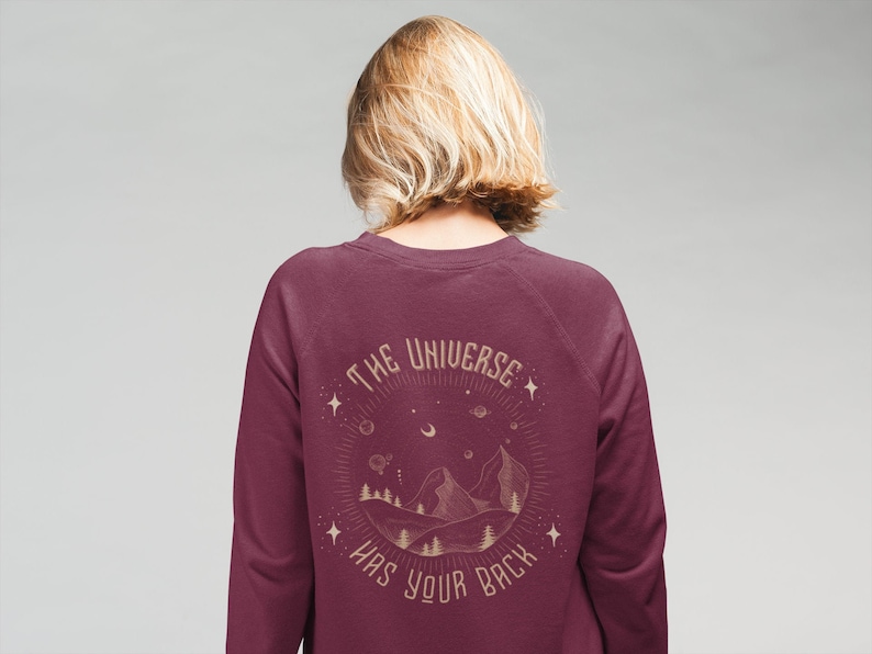 May include: Burgundy sweatshirt with a gold graphic print of a mountain range, stars, and the text "The Universe Has Your Back."