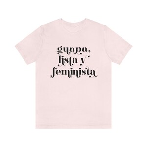 May include: A light pink t-shirt with the words "guapa, lista y feminista" printed in black, stylized font. The shirt is a short-sleeved crew neck style.