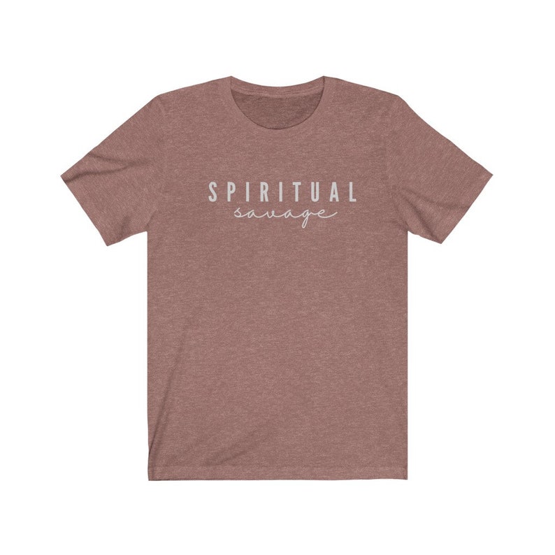 May include: A dusty rose-colored t-shirt with the words "SPIRITUAL savage" printed in a light gray color. The word "spiritual" is in a sans-serif font, and the word "savage" is in a cursive font.