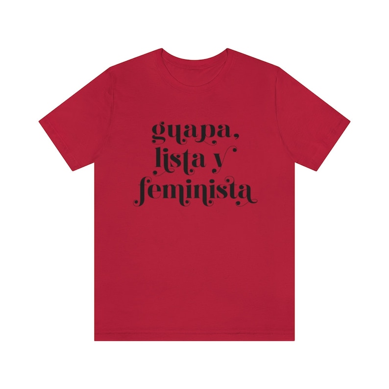 May include: A red t-shirt with the words "guapa, lista y feminista" in black script. The text is centered on the front of the shirt. The shirt has short sleeves and a crew neck.