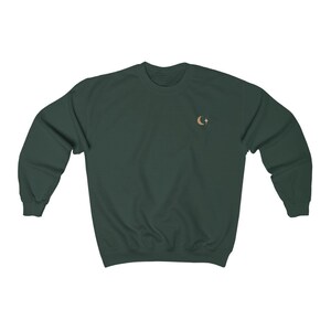 May include: A dark green sweatshirt with a crescent moon and star embroidery on the chest.