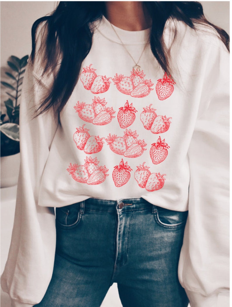 May include: White sweatshirt with a red strawberry print. The strawberries are arranged in a pattern on the front of the sweatshirt.