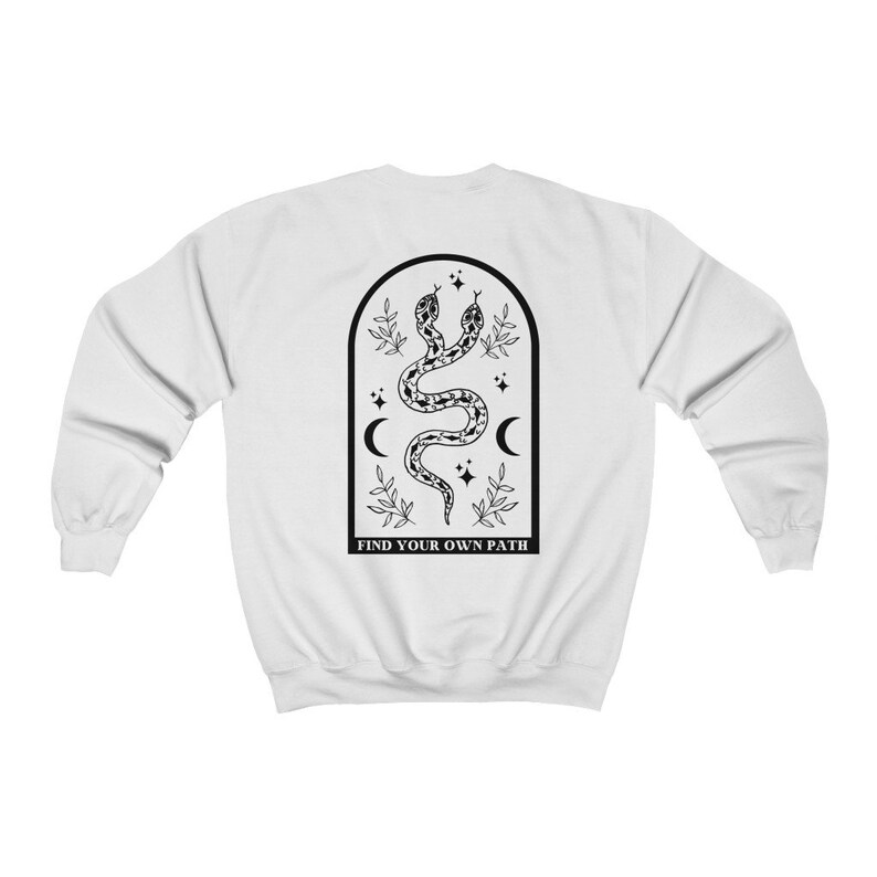 May include: White sweatshirt featuring a black graphic of two intertwined snakes within an arched frame. The design includes crescent moons, stars, and the text "FIND YOUR OWN PATH" at the bottom. The sweatshirt has long sleeves and a crew neck.