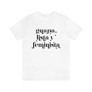 May include: White t-shirt with the text "guapa, lista y feminista" in black script. The shirt is made of a soft material and has a crew neck. The text is centered on the front of the shirt.