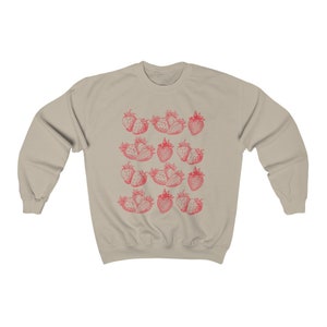 May include: A beige sweatshirt with a red strawberry print. The strawberries are arranged in a repeating pattern across the front of the sweatshirt.