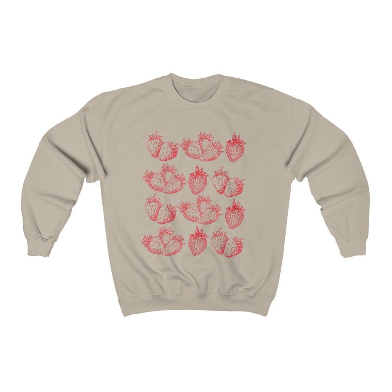 May include: A beige sweatshirt with a red strawberry print. The strawberries are arranged in a repeating pattern across the front of the sweatshirt.