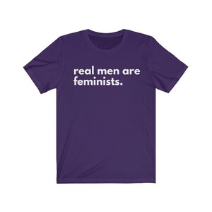 May include: Purple short-sleeved t-shirt with white text that reads "real men are feminists."