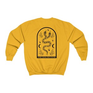 May include: Mustard yellow sweatshirt with a black graphic on the back. The graphic features two snakes intertwined within an arched frame, with crescent moons, stars, and the text "FIND YOUR OWN PATH".