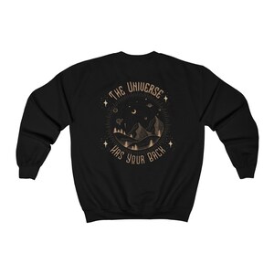 May include: Black sweatshirt with a gold graphic of a mountain range, moon, and stars with the text "The Universe Has Your Back".