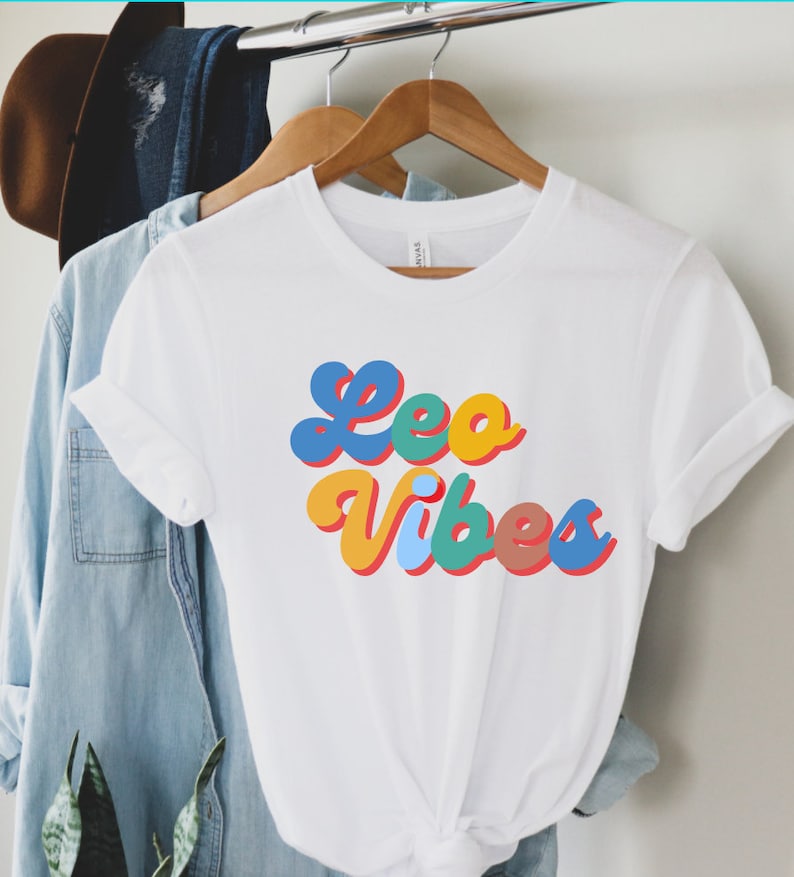Op de afbeelding: Wit T-shirt met een kleurrijke retro-stijl grafische afbeelding met de tekst "Leo Vibes".