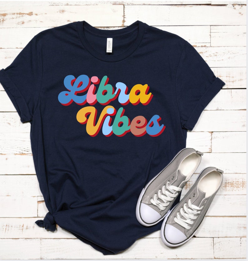 Op de afbeelding: Een marineblauw t-shirt met de tekst "Libra Vibes" in kleurrijke retro letters.