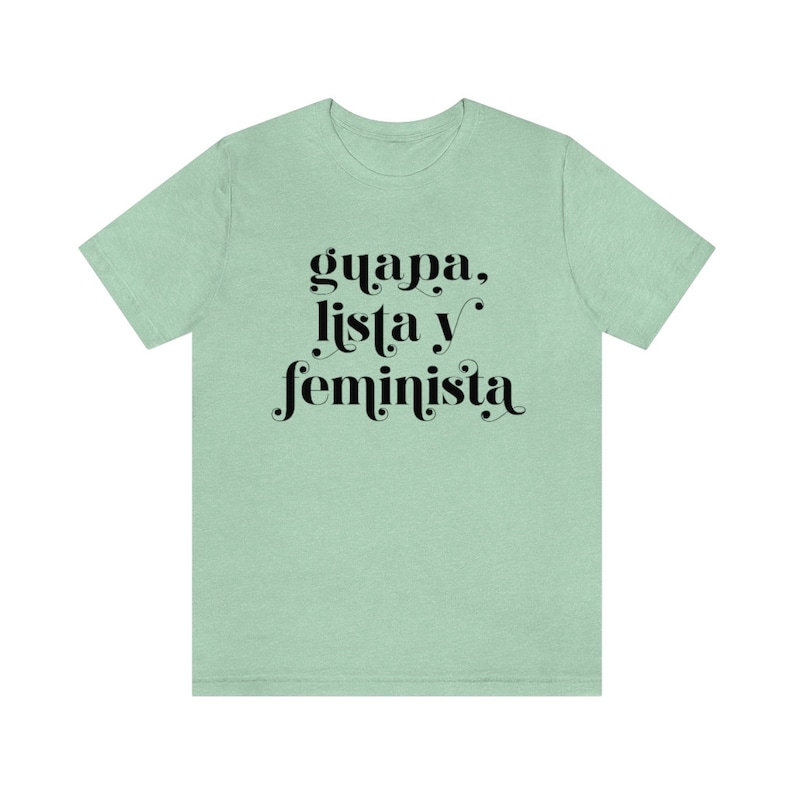 May include: A light green t-shirt with the words "guapa, lista y feminista" in black script. The shirt is a solid color and has short sleeves.