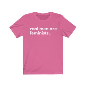 May include: Pink short-sleeved t-shirt with the text "real men are feminists." printed in white.