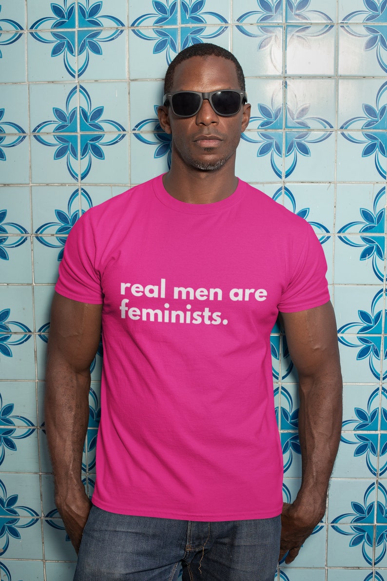 May include: A person wearing a pink t-shirt with the text "real men are feminists." printed in white.