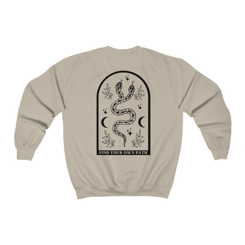 May include: A tan sweatshirt with a black graphic on the back. The graphic features two intertwined snakes within an arched frame, along with moons, stars, and the text "FIND YOUR OWN PATH".