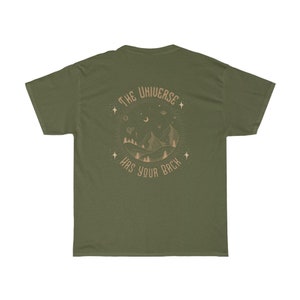 Pode incluir: T-shirt verde-oliva com um gr&aacute;fico circular nas costas. O gr&aacute;fico apresenta montanhas, &aacute;rvores, estrelas e o texto "THE UNIVERSE HAS YOUR BACK" em castanho claro.