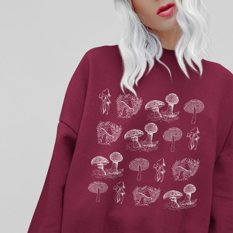 May include: A maroon sweatshirt with a white graphic print of various mushrooms. The mushrooms are drawn in a vintage style.