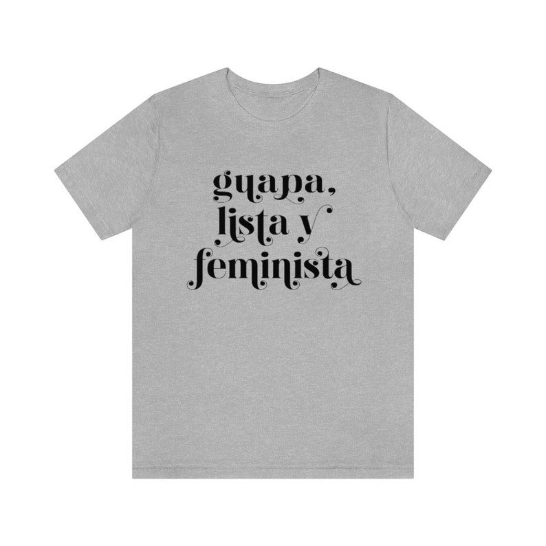 May include: A light gray t-shirt with the words "guapa, lista y feminista" in black script. The text is centered on the front of the shirt. The shirt has short sleeves and a crew neck.