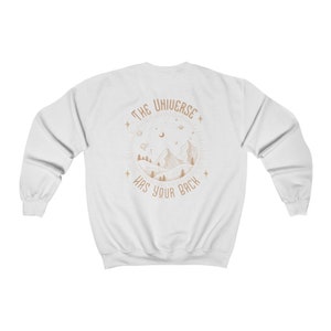 May include: White sweatshirt with a brown graphic of a mountain range with stars and a crescent moon. The text "THE UNIVERSE HAS YOUR BACK" is inside a circle around the mountain range.