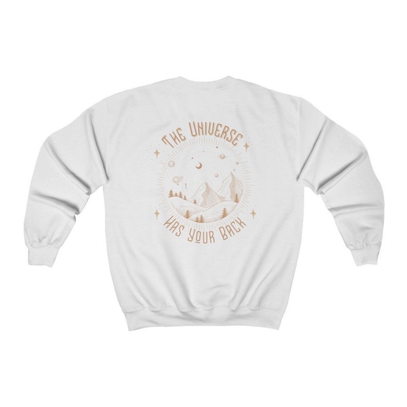 May include: White sweatshirt with a brown graphic of a mountain range with stars and a crescent moon. The text "THE UNIVERSE HAS YOUR BACK" is inside a circle around the mountain range.