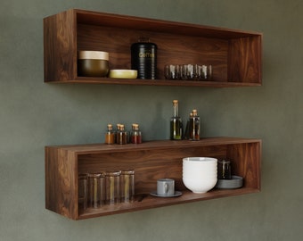 May include: Two wooden floating shelves with a variety of items on them, including glass jars, bottles, a coffee container, and a white bowl. The shelves are mounted on a green wall.