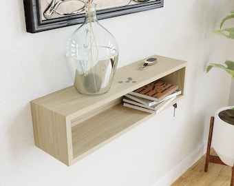 May include: A light wood floating shelf with a rectangular cutout. The shelf is mounted on a white wall and has a vase with dried flowers, a key chain, and a stack of books on it.