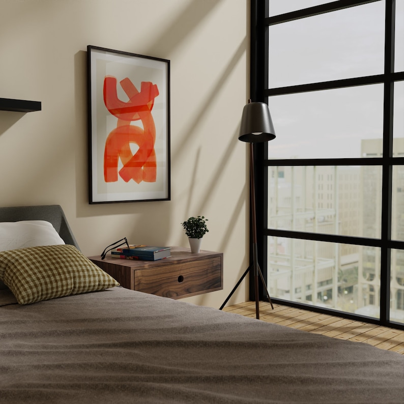 May include: A bedroom with a bed, a bedside table, a lamp, and a window with a view of a city. The bedside table has a book and a pair of glasses on it. The lamp is a black tripod floor lamp with a black shade. The window is large and has black frames. The bed has a brown comforter and a white pillow. There is a small plant on the bedside table.