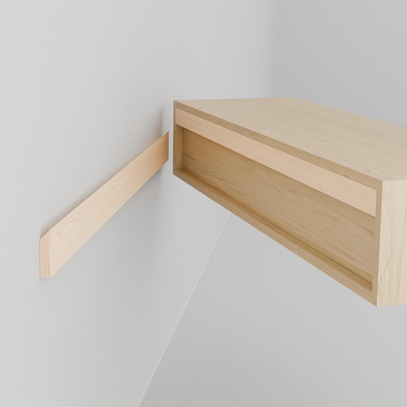 Puede incluir: Una estanter&iacute;a flotante de madera clara con un caj&oacute;n. La estanter&iacute;a est&aacute; montada en una pared blanca con un soporte de madera.