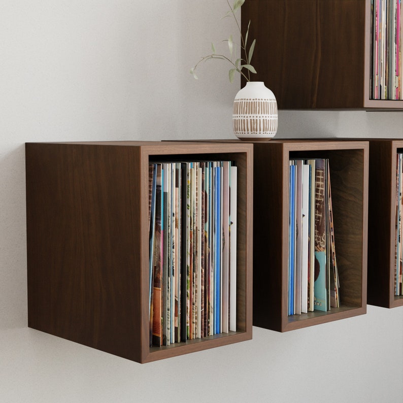 May include: A set of three brown wooden wall mounted shelves with vinyl records displayed on each shelf.