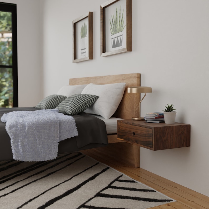 May include: A bedroom with a bed, a nightstand, and a lamp. The bed has a white blanket and black and white pillows. The nightstand is made of wood and has a drawer. The lamp is gold and has a white shade.