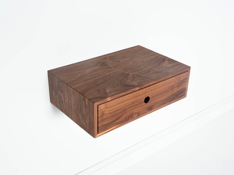May include: A wall-mounted wooden nightstand with a drawer. The nightstand is made of dark walnut wood and has a simple, modern design.