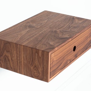 May include: A dark brown wooden wall-mounted shelf with a single drawer. The drawer has a round cutout for a handle.