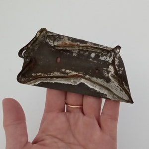 May include: Vintage metal cookie cutter in the shape of a heart with a scalloped edge. The cutter is rusty and has two holes on the top.