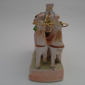 May include: A porcelain figurine of a horse-drawn carriage with a driver in a blue and white hat. The carriage is pink and white with green accents. The horses are white with brown accents.