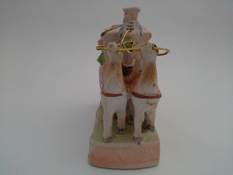 May include: A porcelain figurine of a horse-drawn carriage with a driver in a blue and white hat. The carriage is pink and white with green accents. The horses are white with brown accents.