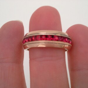 May include: A gold band ring with a row of red gemstones.