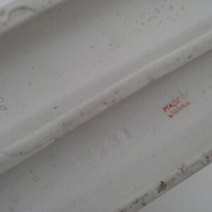 May include: Close-up of the bottom of a white ceramic figurine. The words "MADE IN JAPAN" are printed in red on the bottom.