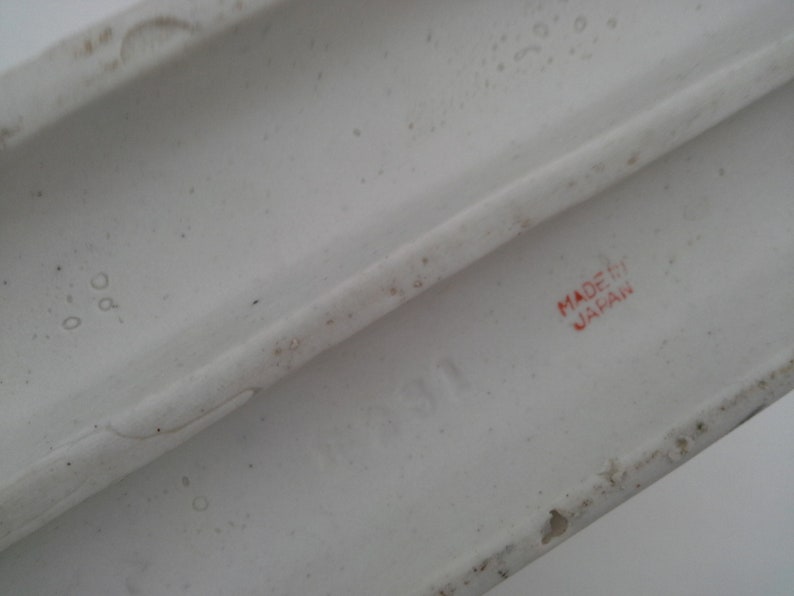 May include: Close-up of the bottom of a white ceramic figurine. The words "MADE IN JAPAN" are printed in red on the bottom.