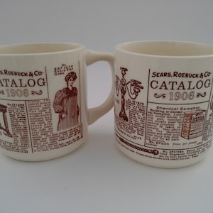 May include: Two white ceramic mugs with brown handles. Both mugs feature a vintage Sears Roebuck & Co. catalog advertisement from 1906. The left mug shows a woman wearing a long dress and the right mug shows a product advertisement for Chemical Camphor.