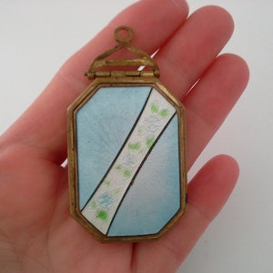 May include: A small, octagonal, blue and white enamel locket with a floral design. The locket has a hinged lid and a brass frame.