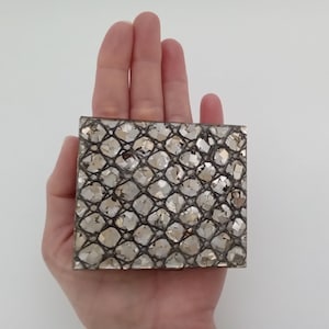 May include: A small, rectangular box with a silver and gold mosaic pattern. The box is made of glass and has a smooth, polished surface.